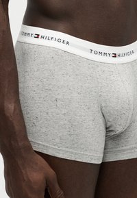 Nærbillede af en mørkhudet mand iført lysegrå Tommy Hilfiger boxershorts med prikmønster.