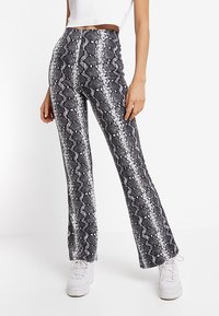 Pantaloni a vita alta con stampa pitone bianca e nera, a zampa d'elefante, con una finitura lucida e dettagli a righe verticali. Indossati con sneakers bianche.