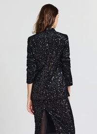 Blazer nero con paillettes, design strutturato, maniche lunghe e dettaglio posteriore con spacco. La texture è liscia e riflette la luce delle paillettes.
