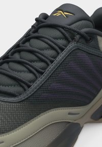 Ciemnoszary sportowy but z wyściełaną siateczkową cholewką, okrągłymi sznurowadłami, fioletowymi akcentami oraz beżową podeszwą z teksturowanym bieżnikiem.