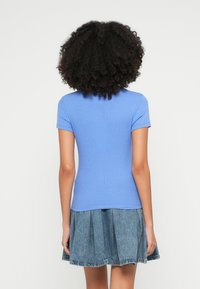 Īsi piedurkņu zils ribots tops ar piegulošu siluetu, kombinēts ar džinsa svārkiem ar pakāpju un uzliesmotu apakšmalu.