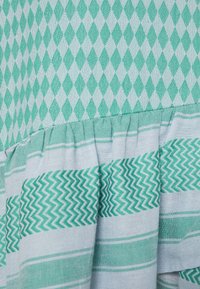 Tela de algodón con un patrón de diamantes en turquesa y azul claro, que presenta un dobladillo con volantes y rayas en zigzag para aportar textura y contraste de diseño.