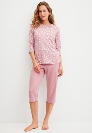 Pyjamセット aus weichem, pinkem Baumwollstoff. Das Oberteil hat ein weißes Herzmuster und 3/4-Ärmel. Die Hose sind passende Capri-Hosen.