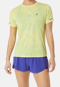 Jasnożółta sportowa koszulka z krótkim rękawem o oddychającej fakturze, wyposażona w wentylację z siateczki, w zestawie z niebieskimi, wzorzystymi spodenki do biegania.