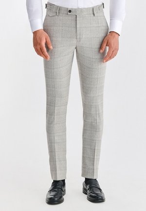 Jasnoszare spodnie w kratę o wąskim kroju, subtelnej fakturze, z pętelkami na pasek i przednimi kieszeniami, zestawione z czarnymi skórzanymi butami.