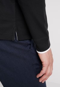 Svart långärmad skjorta med kontrasterande vita manschetter, kombinerad med strukturerade marinblå byxor. Skjortan har sidoflikar för bättre passform.