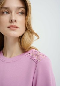 Top rosa realizzato in tessuto morbido, con scollatura rotonda e dettagli in crochet sulle spalle. Design semplice con vestibilità comoda.