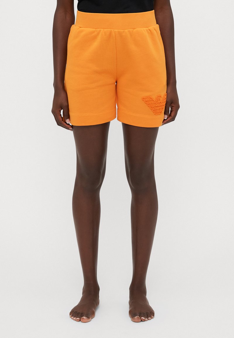 Orange cotton shorts with a ribbed waistband, feature a textured logo detail on the left leg, and a straight cut above the knee.