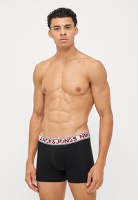 Schwarze Boxershorts mit einem rot-weißen elastischen Bund, der mit "JACK & JONES" Branding versehen ist. Glattes Material, taillierte Passform, mittellanger Schnitt.