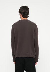 Sudadera de algodón marrón con largas mangas, cuello y dobladillo acanalados; diseño simple, sin patrones ni acentos visibles. Corte clásico.