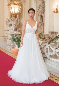 Weißes Brautkleid mit tiefem V-Ausschnitt, Spitzenoberteil und mehrlagigem Tüllrock. Elegantes Design vor neutralem Hintergrund präsentiert.