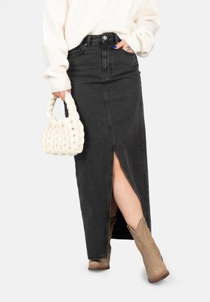 Black denim maxi skirt with front slit, high waist, and belt loops. Paired with a light sweater and a white braided handbag.