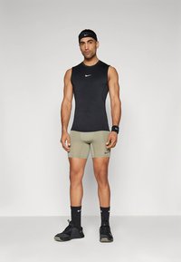 Mustast sporditopsist särgivarrukateta, oliivrohelised lühikesed püksid, mustad sokid ja spordijalatsid. Riietusel ja peapaelal on Nike logod. Tekstuuriga kangas.