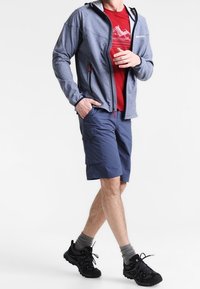 Gray zip-up jacket with hood over red T-shirt, paired with navy shorts and black athletic shoes. Features visible branding and pockets.