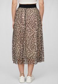 Průhledná béžová maxi sukně s hnědým leopardím potiskem, s elastickým černým pasem a obutými bílými teniskami.