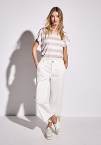 White wide-leg pants paired with a light striped short-sleeve top. Model wears cream sneakers, standing against a plain background.