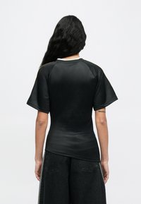 Musta lyhythihainen t-paita pyöreällä pääntiellä ja raglan-hihoilla. Sileä tekstuuri, sisältää minimalistisen suunnittelun ja hienovaraiset kullansävyt.