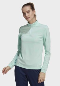 Helles mintgrünes Langarm-Pullover mit einem Viertelreißverschluss, der leicht glänzt, gerippten Bündchen und einem gestickten Logo auf der Brust.