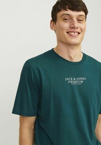 Teal-cotton t-paita, jossa on lyhyet hihat ja pyöreä kaula-aukko. Rintamalla on valkoinen painettu logo "JACK & JONES PREMIUM".