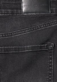 Jean en denim noir montrant les coutures de la poche arrière et une étiquette en cuir noir avec "Street One Studio" embossé.