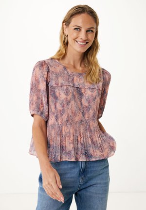 Blouse légère en rose et violet avec un motif texturé, de douces plissures et des manches courtes bouffantes, associée à un jean bleu.