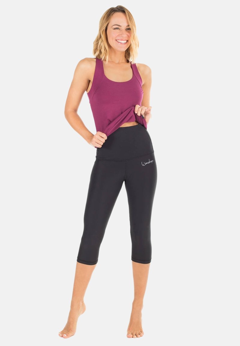 Mörkröd ärmlös topp med en figurnära design, kombinerad med högmidjade svarta caprileggings som har en mjuk yta och diskret logodetalj.