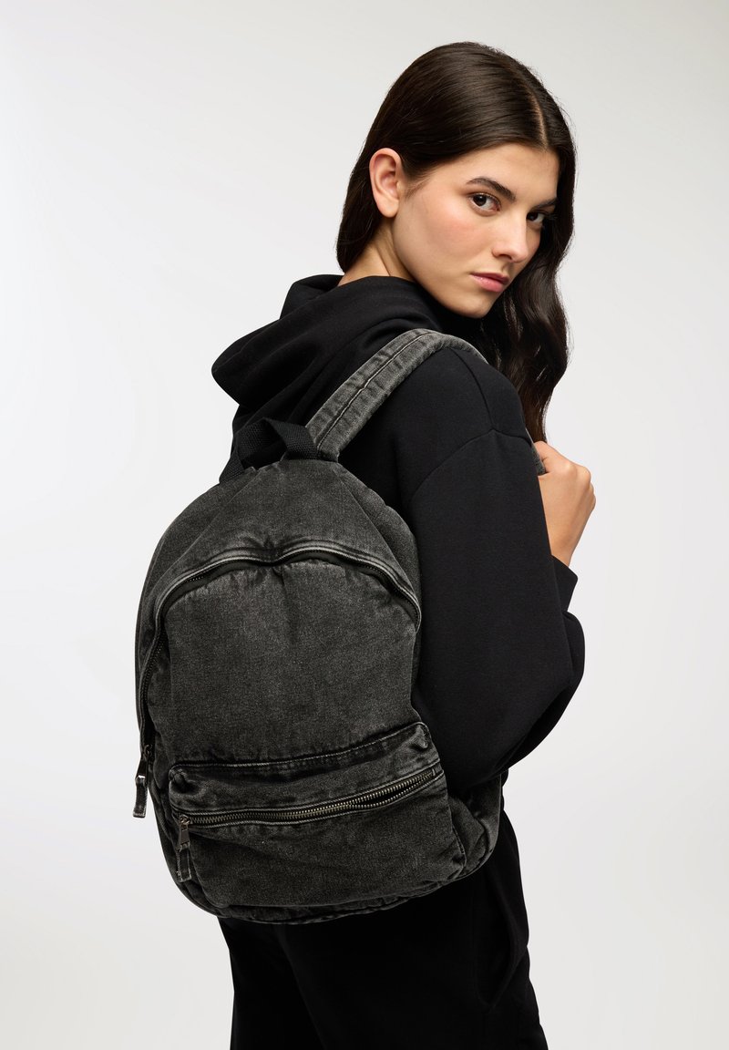 Zaino in denim nero dalla forma arrotondata, con due scomparti con zip e spallacci imbottiti. Il tessuto testurizzato aggiunge un tocco di dettaglio.