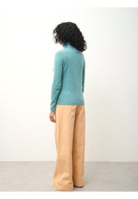 Türkiser Wolle-Rollkragenpullover mit schmal geschnittenem Design, kombiniert mit weiten beigen Hosen aus leichtem Stoff.