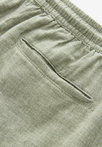 Gros plan sur un short en tissu gris clair texturé avec une taille élastique et une poche arrière horizontale.