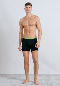 Čierne boxerky s elastickým pásom s logom Nike v zelenej farbe. Materiál je elastický a prispôsobený, zvýrazňujúci tvar tela.