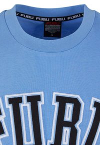 Tricou din bumbac de culoare bleu deschis, cu guler rotund. Prezintă un text mare brodat „FUBU” în negru, conturat în alb. Eticheta din interiorul gulerului indică mărimea „L.”