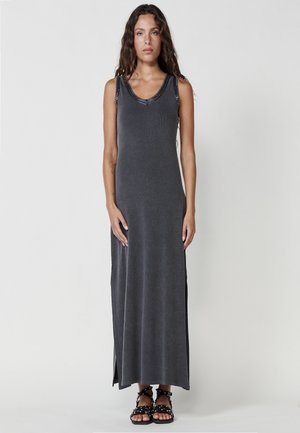 Vestito lungo senza maniche di un grigio scuro, con una texture a coste, dotato di scollo a barchetta e spacchi laterali, abbinato a sandali neri con cinturini.