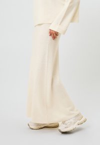 Kaksiosainen asu, jossa on kermaisen värinen pitkähiha-paita ja maksihelmainen hame, yhdistettynä vaaleisiin lenkkareihin. Pehmeä rakenne ja rento istuvuus.