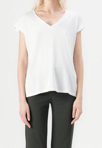 Bílý tričko s výstřihem do V a krátkými rukávy, vyrobené z jemné látky. Jednoduchý design a volný střih, spárované s tmavě zelenými kalhotami.