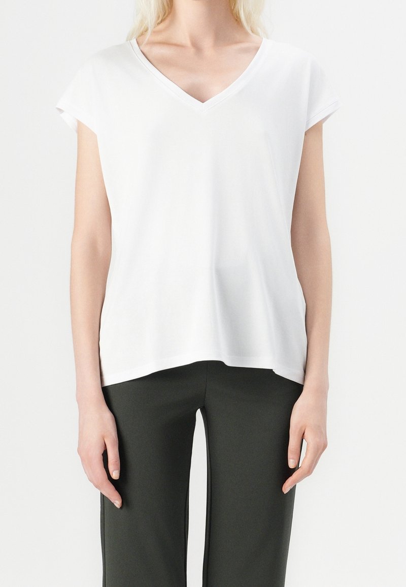 Bílý tričko s výstřihem do V a krátkými rukávy, vyrobené z jemné látky. Jednoduchý design a volný střih, spárované s tmavě zelenými kalhotami.