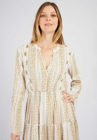 Langarmkleid aus leichtem Stoff mit einem cremigen Grundton, das goldene geometrische und florale Muster, einen V-Ausschnitt und einen gestuften Rock aufweist.
