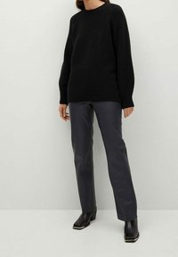 Černý pletený svetr s dlouhými rukávy a kulatým výstřihem; kombinovaný s tmavě šedými fitted kalhotami a kotníčkovými botami se čtveratou špičkou a nízkým podpatkem.