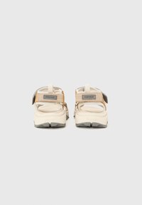 Beige outdoor sandals with adjustable straps, a textured sole, and a curved design, featuring a gray rubber outsole and silver accents.