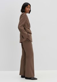 Completo marrone su misura con blazer aderente e pantaloni a gamba larga, realizzato in tessuto liscio, caratterizzato da una vita stretta e linee pulite.