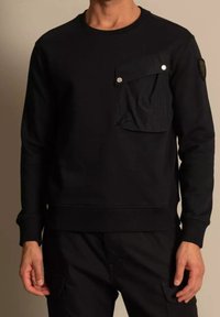 Sudadera negra hecha de tela de mezcla de algodón suave. Cuenta con un bolsillo parche con solapa y cierre de broche en el pecho, así como puños y dobladillo acanalados.