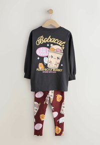 Gray long-sleeve shirt with a cartoon drink graphic; paired with maroon leggings featuring whimsical animal and drink patterns.