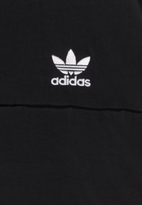 Black fabric with a textured surface, featuring a white embroidered Adidas logo with three leaf-like stripes above the brand name.