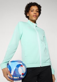 Mint green jacket with a high collar, zip closure, and elastic cuffs, paired with a multicolored soccer ball featuring blue and red accents.