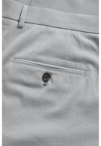 Materialul ușor texturat de culoare gri deschis al pantalonilor prezintă un buzunar din spate cu o închidere cu nasture gri închis și un model de țesătură diagonal subtil.