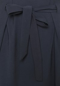 Abito navy con una cintura larga e un dettaglio a nodo legato. Il tessuto ha una texture liscia con plissettature sui lati.