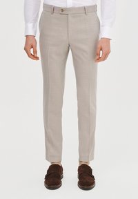 Jasnoszare, dopasowane spodnie o delikatnej teksturze, z pojedynczym zapięciem na guzik i wąskim kroju. Połączone z ciemnobrązowymi zamszowymi butami.