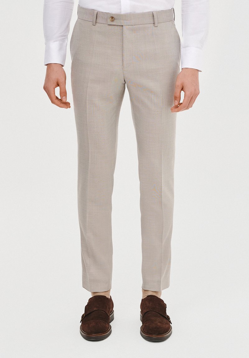 Jasnoszare, dopasowane spodnie o delikatnej teksturze, z pojedynczym zapięciem na guzik i wąskim kroju. Połączone z ciemnobrązowymi zamszowymi butami.