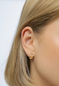 Boucle d'oreille en or avec un design texturé et martelé, présentée sur l'oreille d'un modèle, sur fond blanc uni.