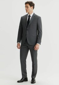 Szary garnitur w kratę o slim fit, z zapięciem na dwa guziki, klapami w szpic oraz bocznymi kieszeniami. Połączony z czarnymi eleganckimi butami.