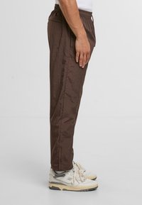 Brązowe, lekkie spodnie nylonowe z elastycznym paskiem, kieszeniami bocznymi i luźnym krojem, w zestawie z białymi trampkami.
